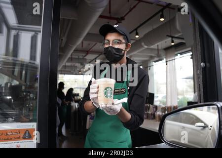Starbucks Mitarbeiter geben Befehle mit fröhlichem Gesichtsausdruck und tragen eine Gesichtsmaske am Drive-in. Eisgekühlter weißer Mokka-Kaffee. Stockfoto