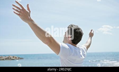 Junger lateinamerikanischer Mann atmet mit offenen Armen am Strand Stockfoto
