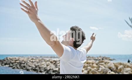Junger lateinamerikanischer Mann atmet mit offenen Armen am Strand Stockfoto