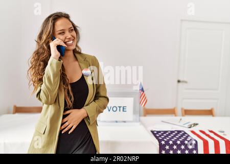 Junge, wunderschöne hispanische Frau, Wahlpräsidentin, die auf dem Wahlcollege mit einem Smartphone spricht Stockfoto