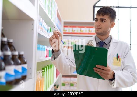 Junger hispanischer Apotheker, der in der Apotheke auf das Klemmbrett schreibt Stockfoto