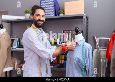 Ein junger, hispanischer Schneider, der bei der Prüfpuppe steht und im Atelier arbeitet Stockfoto