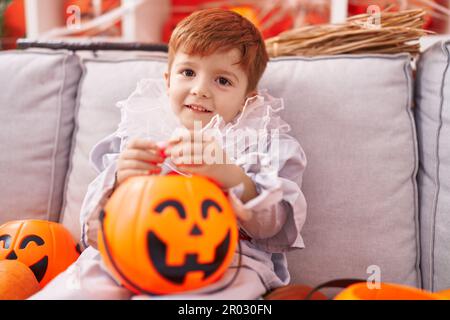 Ein niedliches Kleinkind, das zu Hause ein Harlequin-Kostüm trägt und einen Kürbiskorb hält Stockfoto