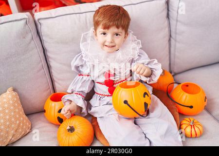Ein niedliches Kleinkind, das zu Hause ein Harlequin-Kostüm trägt und einen Kürbiskorb hält Stockfoto