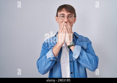Ein blonder, weißer Mann mit Brille, lachend und peinlich kichernd, der den Mund mit Händen, Klatsch und Skandal verdeckt Stockfoto