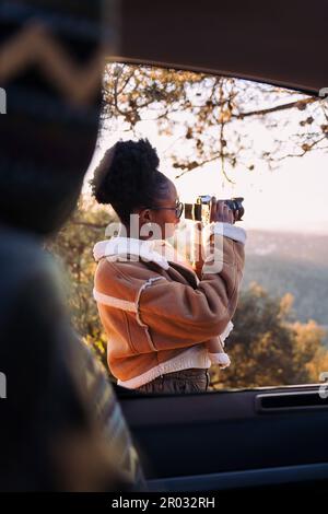 Junge afrikanerin, die während eines Roadtrips im Wohnmobil mit einer Kamera Fotos von der Natur macht, Konzept des Lebens im Minibus und Reiseabenteuer Stockfoto