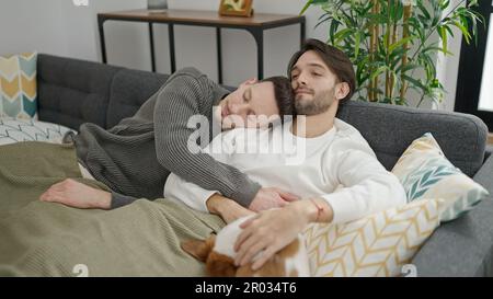 Zwei Männer, die sich zu Hause auf dem Sofa mit einem Hund umarmen Stockfoto