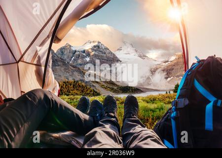 Wanderbeine eines Paares, die sich in einem Zelt mit Blick auf die Rocky Mountains im Nationalpark von BC, Kanada, entspannen Stockfoto