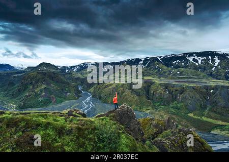 Majestätische stimmungsvolle Landschaft mit erfolgreichem Wanderer, der im Sommer auf dem Valahnukur Trail zwischen zerklüfteten Vulkanbergen im isländischen Hochland Thorsmork steht Stockfoto