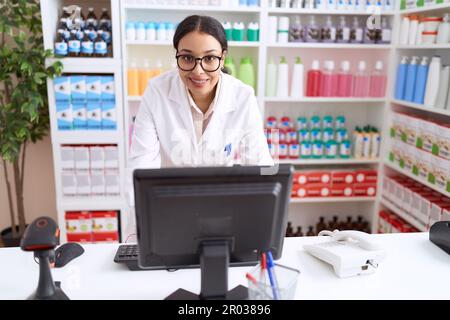 Junge arabische Apothekerin, die selbstbewusst mit dem Computer in der Apotheke lächelt Stockfoto