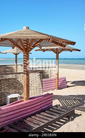 Sonnenschirme aus Holz, Sonnenliegen und Windschutzscheiben am Strand. Stockfoto