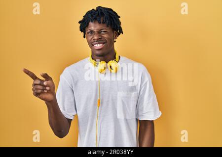 Junger afrikanischer Mann mit Dreadlocks, die auf gelbem Hintergrund stehen und zur Seite zeigen, besorgt und nervös mit dem Zeigefinger, besorgt und überrascht, Expressi Stockfoto