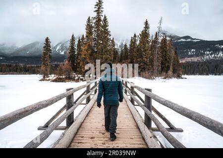 Ein Mann, der im Winter auf einer Holzbrücke zwischen dem gefrorenen See im Pyramid Lake im Jasper-Nationalpark, ab, Kanada, spaziert Stockfoto