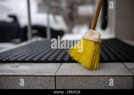 Eine Aufnahme eines Besens mit Holzgriff, der auf dem Boden vor einer schwarzen Fußmatte stand Stockfoto