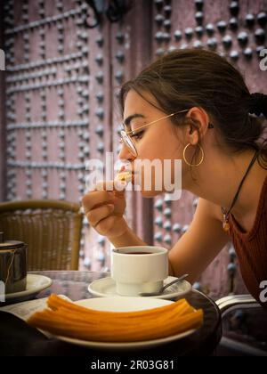 Das junge Mädchen isst einen Snack Churros und eine Tasse heiße Schokolade Stockfoto