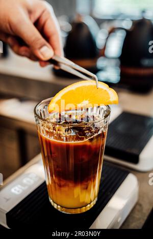 Ein frisch zubereitetes kaltes Getränk aus Kaffee und Orangensaft, das in ein großes Glas über Eiswürfeln gegossen wird Stockfoto