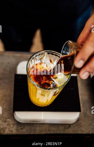 Ein frisch zubereitetes kaltes Getränk aus Kaffee und Orangensaft, das in ein großes Glas über Eiswürfeln gegossen wird Stockfoto