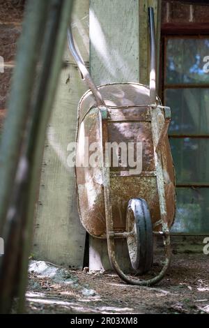 Alte rostige Schubkarre an der Hauswand. Stockfoto