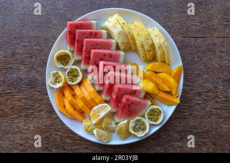 Tropische Früchte auf einem Frühstücksteller, aus nächster Nähe, Blick von oben. Frische Wassermelone, Passionsfrucht, Ananas, Mango, Papaya, Orange zum Essen im Strandrestaurant Stockfoto