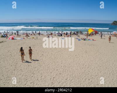 Tauranga Neuseeland - 12 2011. Februar; zwei junge Frauen mit Bikinizone laufen am Sommertag in Richtung des überfüllten Hauptstrands am Mount Maunganui Stockfoto