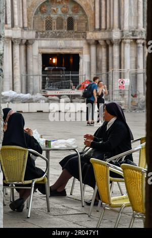 Kleine Gruppe von Nonnen, die im Caffè Lavena auf dem Markusplatz sitzen, mit der Basilika im Hintergrund, Venedig, Venetien, Italien Stockfoto