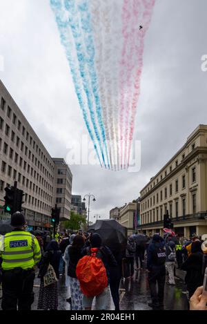 Rote Pfeile fliegen bei der Krönung von König Karl III. Über den Strand in Richtung Buckingham Palace, London, Großbritannien. Leute im Regen beobachten Stockfoto