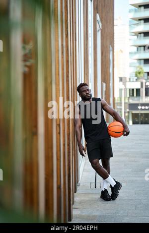 Starker, sportlicher junger schwarzer Mann, der den Basketballball draußen hält. Stockfoto