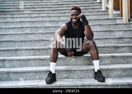 Passend für den sportlichen Boxer mit schwarzem Boxer, der draußen auf der urbanen Treppe sitzt. Stockfoto