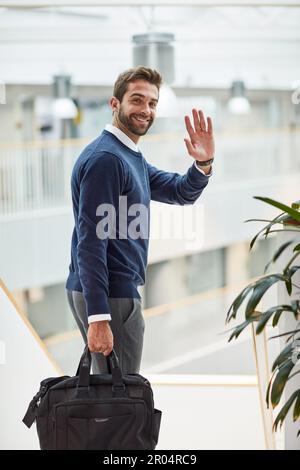 Bis zum nächsten großen Erfolg. Porträt eines jungen Geschäftsmannes, der winkt, während er eine Tasche trägt. Stockfoto