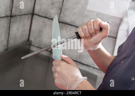 Der Koch schärft das Küchenmesser mit musat. Hochwertiges Foto Stockfoto