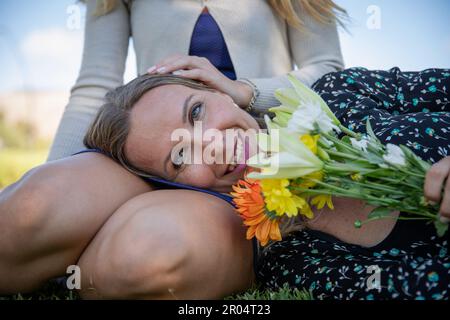 Eine Mutter mit Blumen, die ihren Kopf auf den Beinen ihrer Tochter ruht Stockfoto