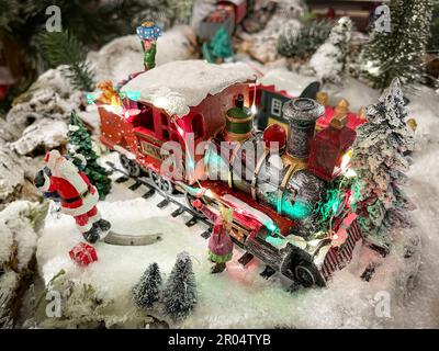 weihnachtsszene mit Miniaturfiguren und einer Lokomotive mit Geschenken neben dem weihnachtsmann in einer verschneiten Landschaft, selektiver Fokus, horizontal Stockfoto