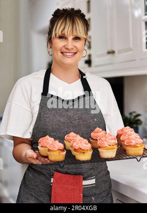 Verkaufen Sie Ihre Backwaren von zu Hause aus. Eine Frau, die zu Hause frisch gebackene Cupcakes in der Küche hält. Stockfoto