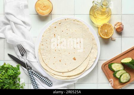 Teller mit frischem Lavash, Gurke, Öl und Sauce auf weißem Fliesenhintergrund Stockfoto