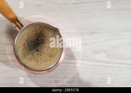 Cezve mit heißem, aromatischem türkischem Kaffee auf weißem Holztisch, Blick von oben. Platz für Text Stockfoto