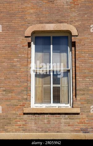 Nahaufnahme des Texturhintergrunds einer orangefarbenen und beigen Backsteinwand mit verwitterten Ziegeln und einem Holzfenster mit Backsteinrahmen Stockfoto