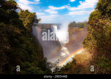 Ein doppelter Regenbogen bildet sich, während der Sambesi über die spektakulären Victoria Falls in eine Schlucht stürzt, die Simbabwe und Sambia trennt Stockfoto