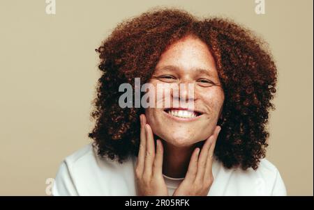 Glücklicher junger Mann, der selbstbewusst lächelt, während er seine natürliche Schönheit umarmt und pflegt. Ein Mann mit Sommersprossen, der sein makelloses und einzigartiges Gesicht bewundert Stockfoto