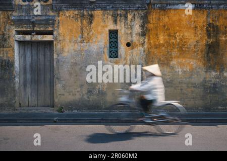 Vietnamesische Frau mit traditionellem Hutfahrrad in der Altstadt. Stadtleben in Hoi an, Vietnam. Stockfoto