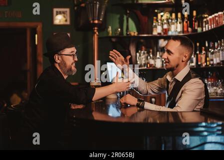 Der Mann hat Spaß, sich mit einem Barkeeper an der Bar bei einem Glas Bier in einem Pub zu unterhalten Stockfoto