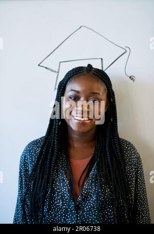 Ich will meine Eltern stolz machen. Abgeschnittenes Porträt eines jungen Universitätsstudenten, der gegen ein Whiteboard steht, auf dem eine Abschlussmütze gezeichnet ist. Stockfoto