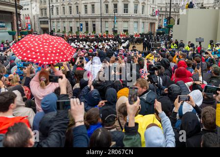 Die Menschenmassen stehen im Regen, um einen Blick auf die königliche Prozession zur Krönung von König Karl III. Zu werfen Leute in der Nähe von Trafalgar Square, London Stockfoto