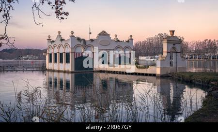 Die ruhige Schönheit des Banyoles Lake spiegelt sich in der Dämmerung am Himmel wider, eingerahmt von einem majestätischen Bauwerk und umgeben von Bäumen. Stockfoto