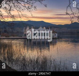 Die ruhige Schönheit des Banyoles Lake spiegelt sich in der Dämmerung am Himmel wider, eingerahmt von einem majestätischen Bauwerk und umgeben von Bäumen. Stockfoto