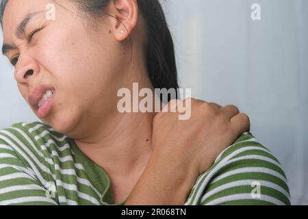 Eine mürrische junge Frau, die ihren Hals hält. Müde Frau massiert steifen Nacken, anstrengende Muskeln, erschöpft von der Arbeit. Oberarmschmerzen. Gesundheitswesen Und Medizin Stockfoto