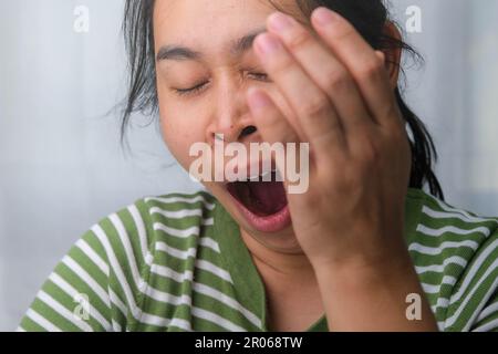 Müde Frau, die ihren Mund mit ihren Händen bedeckt und sich ausruhen will. Porträt einer asiatischen Frau mit negativem Gesichtsausdruck, müde, gähnend, bedeckt sie Stockfoto