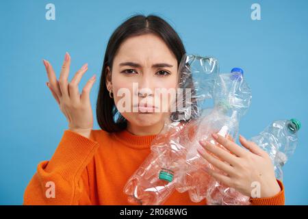 Frau mit wütendem Gesicht, Flaschen in der Hand, Plastikabfall recyceln, sich beschweren, auf blauem Hintergrund stehen Stockfoto