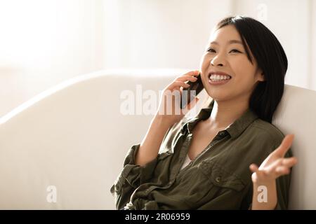 Lachende, wunderschöne asiatische Frau, die zu Hause telefoniert Stockfoto