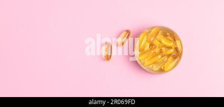 Gelbe transparente Kapseln, Nahrungsergänzungsmittel mit Fischöl auf rosa Hintergrund. Gesundheitswesen, Pharma-Webbanner. Stockfoto