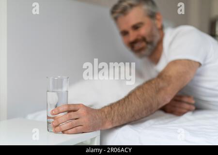 Ein Mann mittleren Alters, der ein Glas Wasser auf dem Nachttisch erreicht Stockfoto